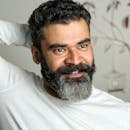 Close-up portrait of a smiling bearded man in a white shirt with a blurred background.
